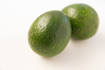 Couple of two whole avocado fruits with peel. Closeup shot. Isolated objects on white background. Fresh food or healthy diet concept