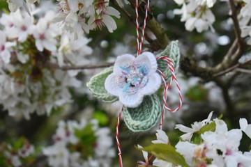 Handmade crocheted flower, with a red and white string, known as Martisor, on a blossoming cherry...
