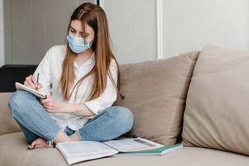 woman at home on couch wearing mask studying with books and notebook