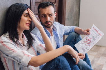 Stressed woman with husband holding document with foreclosure and final notice lettering on floor in room