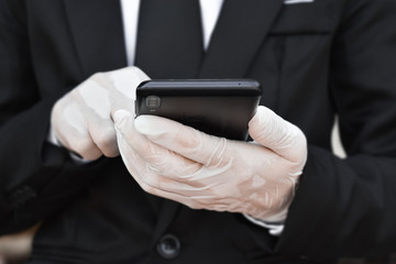 Close up of  businessman wearing white latex gloves are using smartphone. Concept for work prevent health from corona virus or covid-19.