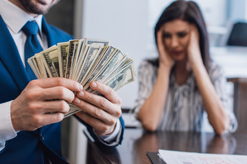Selective focus of collector with money near stressed woman at table in room - obrazy, fototapety, plakaty