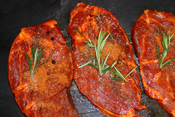 juicy marinated with spices raw meat on a black board, steaks with rosemary, the concept of protein nutrition, diet, barbecue party, cooking homemade food
