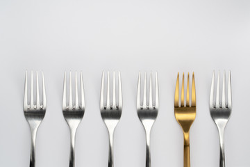 One gold fork and five silver forks on the white background. Be different. Think outside the box concept. Top view.