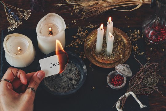 Female wiccan witch holding a burning peace of paper in her hand. White paper with I wish written on it. Casting a spell for wish to come true, sending thoughts into the Universe, dream manifestation