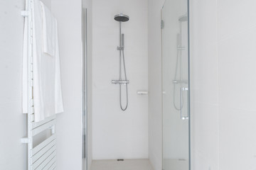 White bathroom shower with a glass reflection and white towel hanging on a wall