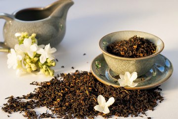 Dry green tea herbs with flowers and vintage porcelain plate and milk jug on white background.