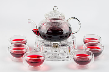 Red tea in teapot on stand with candle and glass cups on white background.