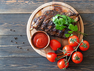 Hot grilled and smoked spare ribs. BBQ served with a fresh tomatoes on a round wooden cutting board