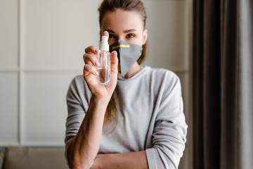 woman holding hand sanitizer wearing respirator mask at home