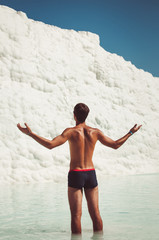 Man stand on a white mountain in Pamukkale. Young tourist man admiringly raising his hands looks at an travertine pools