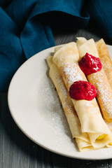 Pancakes with custard and raspberry sauce, dark wooden background, selective focus