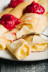 Pancakes with custard and raspberry sauce, dark wooden background, selective focus