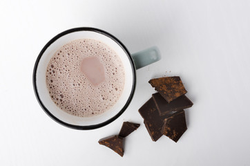 Top view of mug of delicious hot cocoa drink and pieces of dark chocolate on the white background