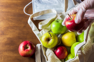 Hand in glove holds apple. Eco mesh bag with food supplies on a wooden background. Food delivery in eco-friendly packaging, zero waste.
