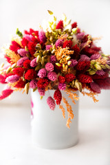 Vertical picture of many colourful artificial synthetic flowers of red, pink, purple, white and orange colors, bouquet in vase on white window sell. Graphic floral design