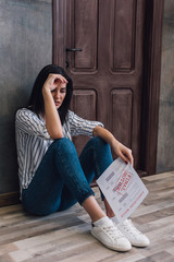Worried woman holding document with foreclosure and final notice lettering and sitting near wall on floor in room - obrazy, fototapety, plakaty