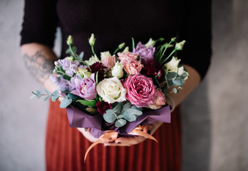 Very nice young woman holding big beautiful blossoming bouquet of fresh roses, carnations, eustoma, chrysanthemum, calla lilies flowers in pink and purple colors on the grey wall background