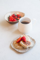 Tasty and freshly prepared breakfast with pancakes, strawberries and a cup of coffee on a white background.