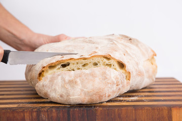 Side view of cutting of freshly baked homemade round bread in slices. Isolated object on white background. Healthy food for breakfast concept