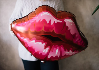 Young woman holding inflatable lips balloon on the grey wall background