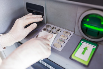 Hands in surgical rubber gloves sanitizing atm machine buttons with wet wipe, covid-19 prevention.