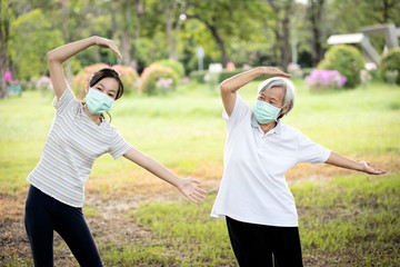Happy child girl is doing exercise activity for the old elderly,healthy senior woman workout and wear face mask outside home after Coronavirus quarantine or Covid-19 lockdown,work out for health care