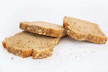Three slices of cereal bread with seeds. Crumbs laying around. Rustic rye loaf sliced pieces isolated on white background. Studio shot. Side view. Home culinary and baking concept