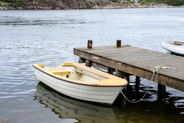 Obraz premium Wooden white boat parking on the wood pier on water with reflection background, Sweden.
