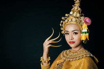 Beautiful Asian woman wearing golden traditional Thai performance dancer dress with headgear jewelry and long nails on black background isolated.