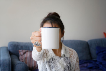 Woman holding white coffee cup to camera in room background