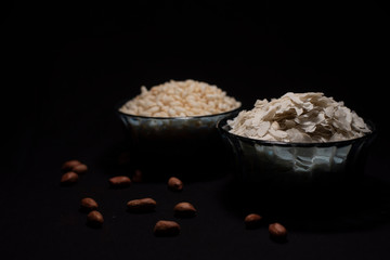 Two bowls full of puffed rice and rice cereals decorated with scattered peanuts in a dark copy space background. Food and product photography.