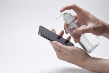 Fototapeta premium Disinfection of the phone. Hands hold smartphone and bottle or container for antiseptic cream or gel white background.