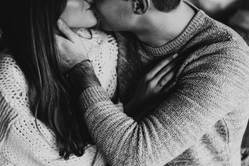 Black and white photo. Couple on the bed in the bedroom. Dark interior. New Year's and Christmas. Hugs and kisses. Love. White sweater and high socks. Romantic meeting. A date lovers.