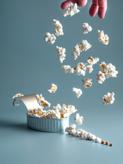 male hand dropping popcorn on a tin, isolated on gray background