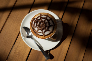 a Cup of coffee cappuccino on a wooden table top view drawing on the foam in the form of a web