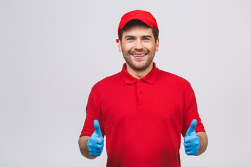 Portrait of attractive delivery man in red t-shirt and cap smiling and showing thumb up isolated over red background.