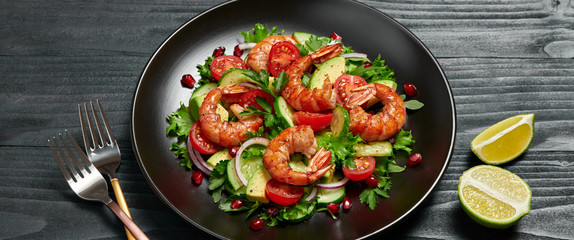 Shrimps salad, avocado, lettuce, cherry tomatoes. Homemade vegetarian shrimp salad. Seafood concept. Mixed leaves, grilled prawn shrimps in plate on black wood background, banner