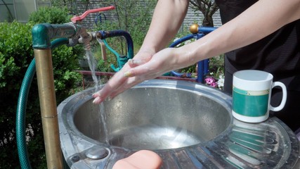 A woman thoroughly washes her hands with soap in the yard of her house.