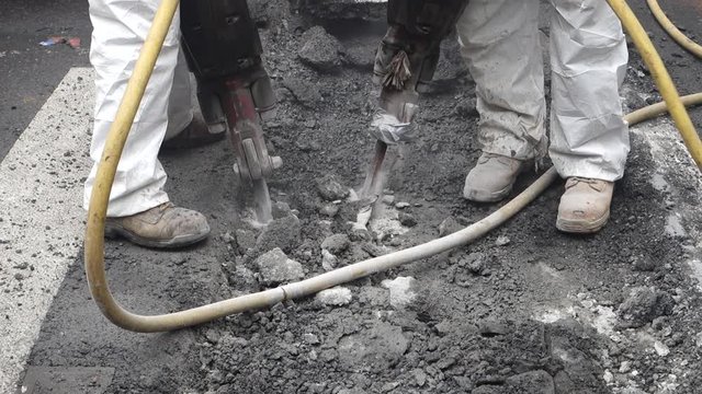 two men with very noisy loud jackhammers,  jackhammerinat a sidewalk street construction site