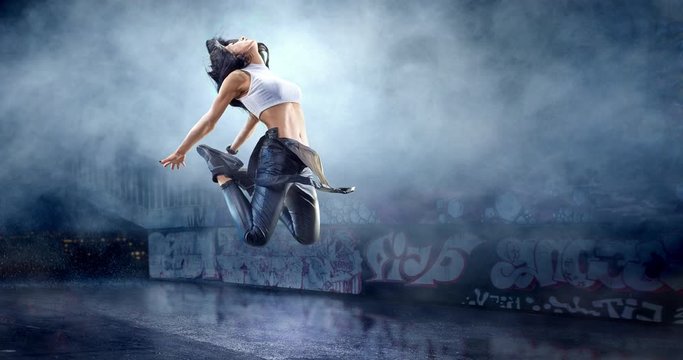 Female street dancer in a jump with a graffity wall behind the fog on a backgroung.