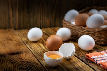 Farm eggs white and brown lie on a wooden table and in a basket, close-up, low light, selective focus, shallow depth of field. Organic food concept