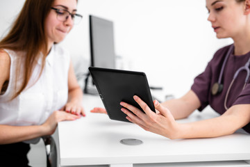 Close up of female doctor and patient sitting at the desk in modern clinic.