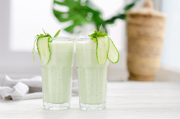 Refreshing fermented milk drink with cucumber and herbs. Two with such a cocktail in a light interior on a white table.