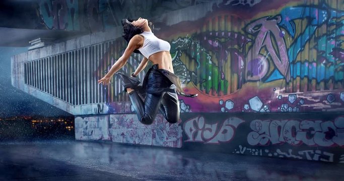 Female street dancer in a jump with a graffity wall on a backgroung.
