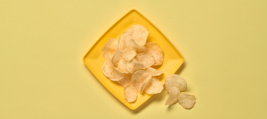 Potato chips on plate, minimal. Vegan beer snack on yellow background. Crispy veggie chip, creative monochrome yellow concept. Home made potato crisps, top view