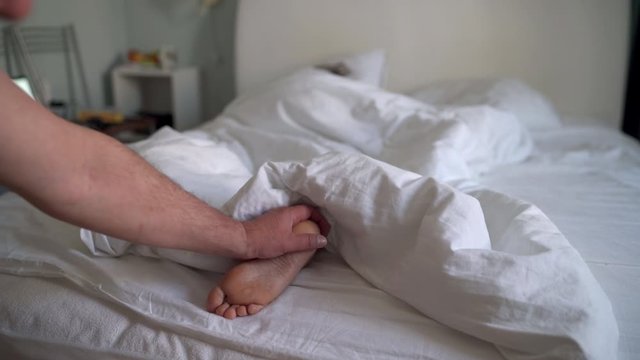 Woman sleeping in bed under white blanket, man touching womans bare feet.