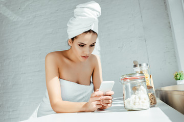 Beautiful woman wrapped in towels using smartphone in kitchen