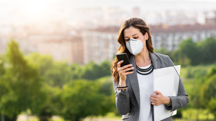 Young businesswoman wearing face mask outside during Covid-19 coronavirus health crisis. Professional woman using her smartphone.