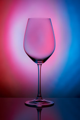 The crystal glass stands on the reflecting surface on a pink blue background. studio photo. product. Beautiful shadow from wine glass. macro photo